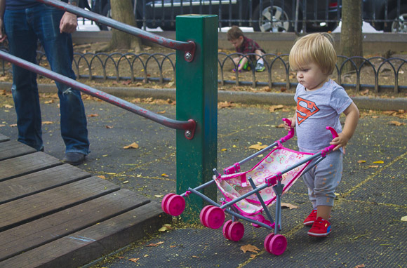 A boy pushes a pink stroller up a wood ramp