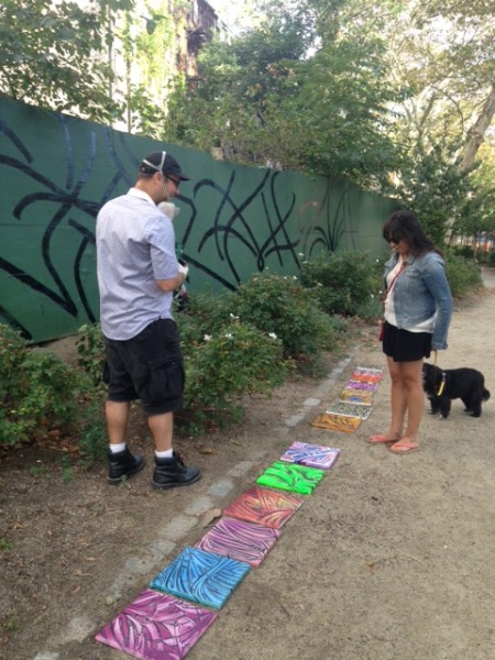 Cram Concepts talks to a woman walking in the park about his paintings for sale.  Shannon Luibrand/NYCityLens