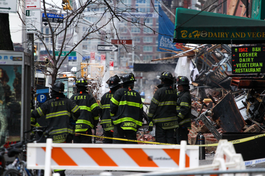 Firefighters stand near what's left of three buildings. (Solange Uwimana / NY City Lens)