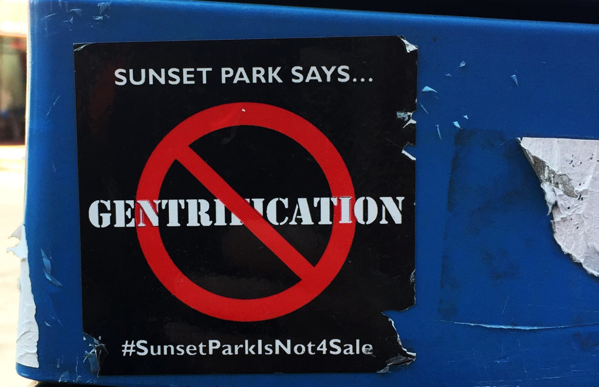 A sticker against gentrification on the side of a parking meter along Fifth Avenue in Sunset Park