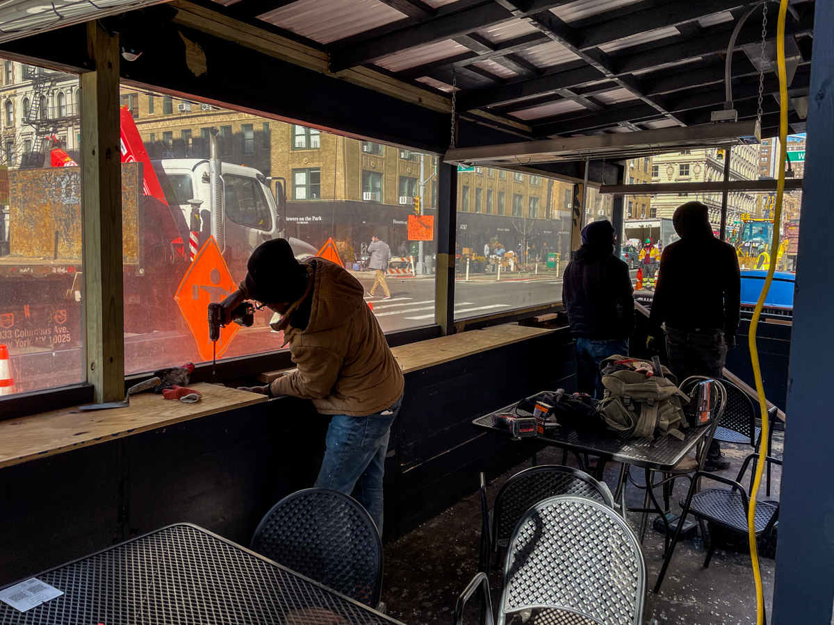 Workers repair an outdoor dining shed at the corner of 85th street and Amsterdam avenue on Manhattan's Upper West Side on Feb. 9, 2022. The Department of Transportation said on Tuesday it does not envision sheds in outdoor dining's post-Covid future. Credit: Luke Cregan for NY City Lens.