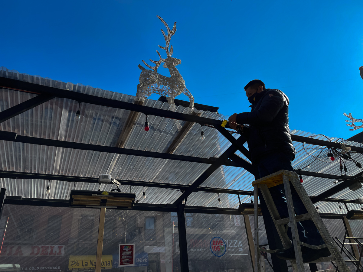 A man repairs lights on an outdoor dining shed on Manhattan's Upper West Side on Feb. 9, 2022. The Department of Transportation said on Tuesday it does not envision sheds in outdoor dining's post-Covid future. Credit: Luke Cregan for NY City Lens.